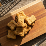 Peanut Butter & Banana Dog Biscuits (Nalla's Sunday Batch) — Overhead natural food photography of a small pile of golden-brown peanut butter and…