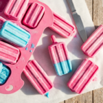 Berry & Yogurt Swirl Frozen Pupsicles — An overhead shot of vibrant pink and blue swirled frozen pupsicles in a silicone mold,…